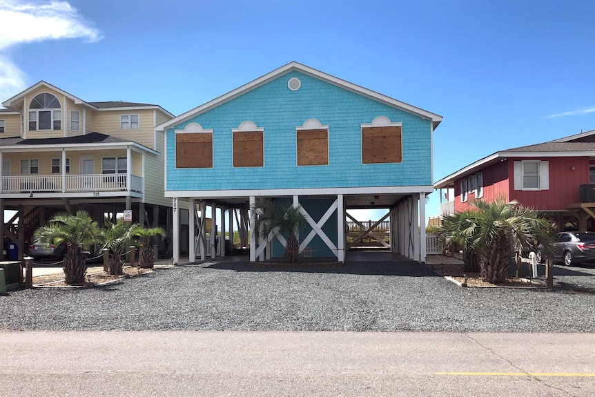 A blue house on stilts with boarded up windows