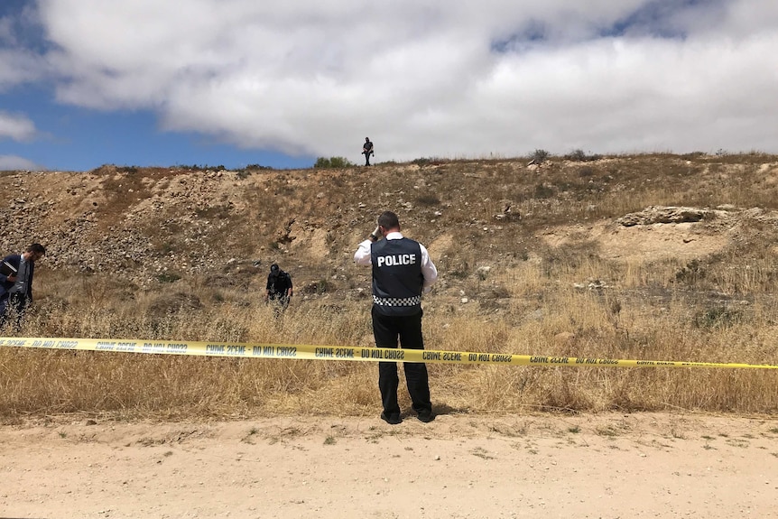 Four police officers search an area of land for clues.