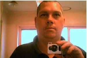 A man with a short hair cut holds a camera in the mirror taking a "selfie" photo