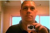 A man with a short hair cut holds a camera in the mirror taking a "selfie" photo