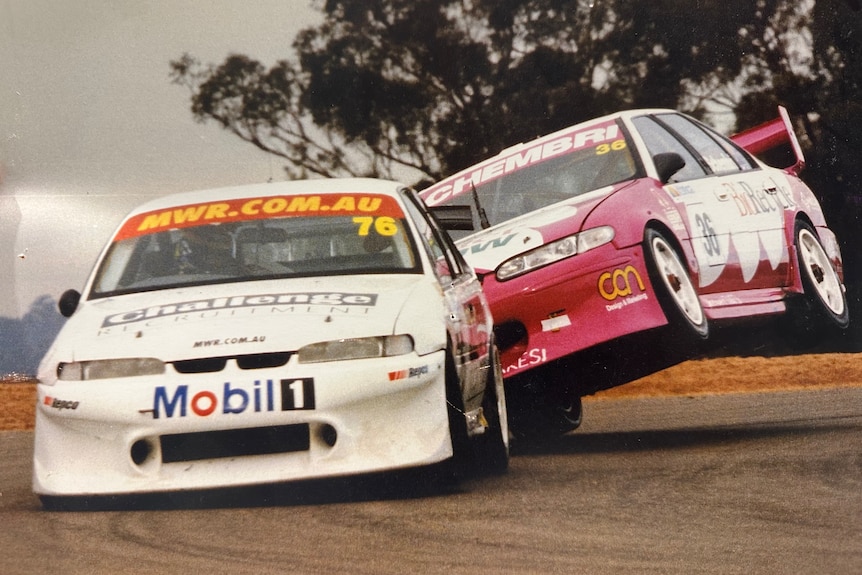 Two cars on a race track, one of which is up on two wheels.