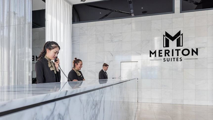 Three receptionists in fancy uniforms behind a marble reception desk at the Meriton Suites.