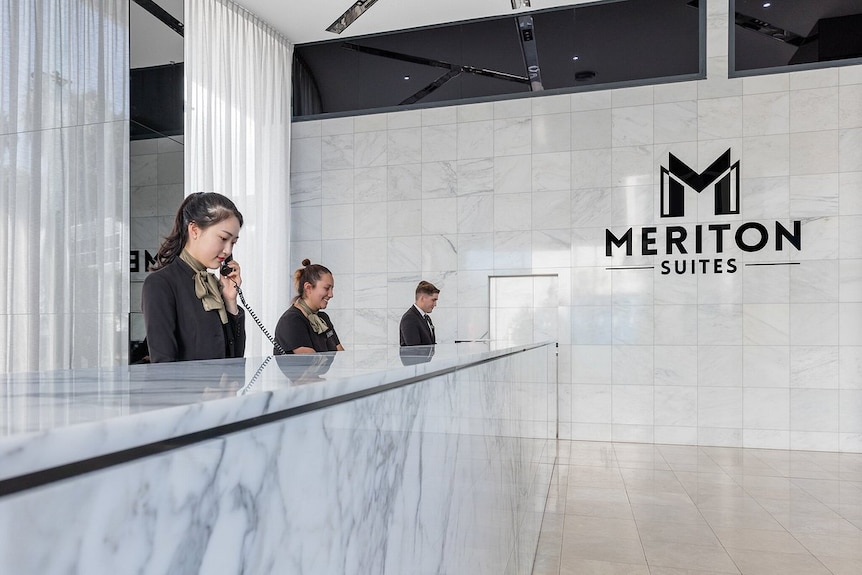 Three receptionists in fancy uniforms behind a marble reception desk at the Meriton Suites.