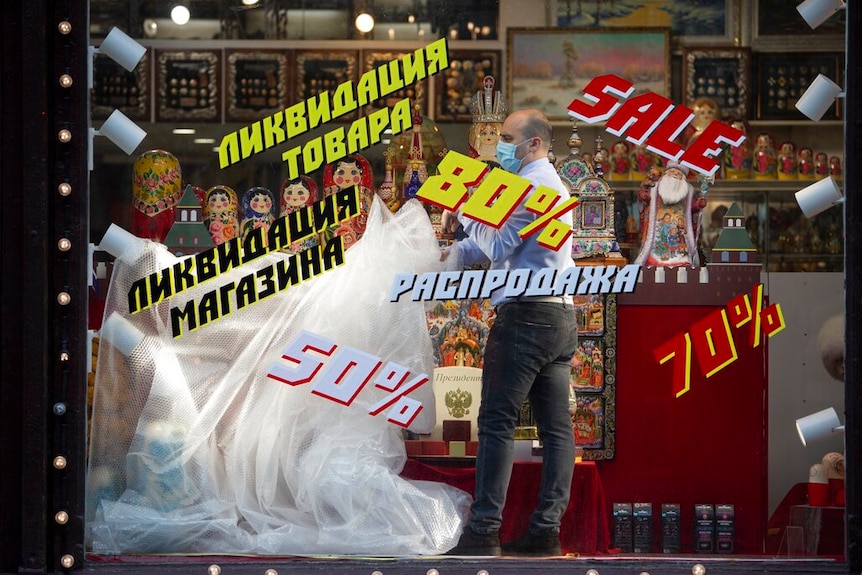 Looking through a toy shop window with bright Russian words written over it, you see a man unfurl bubble wrap.