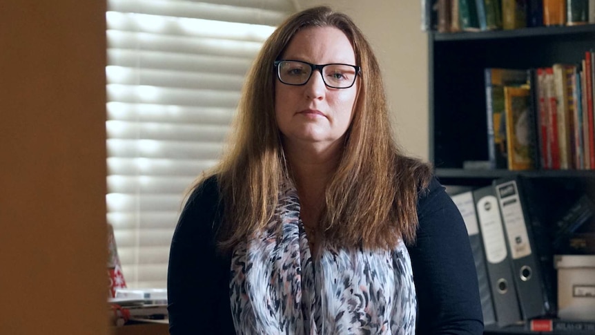 A woman in glasses sits in a home study.