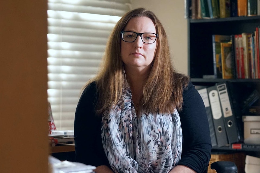 A woman in glasses sits in a home study.