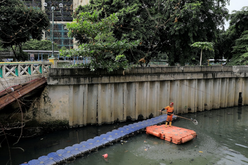 A municipal worker wearing orange cleans a polluted canal in Jakarta