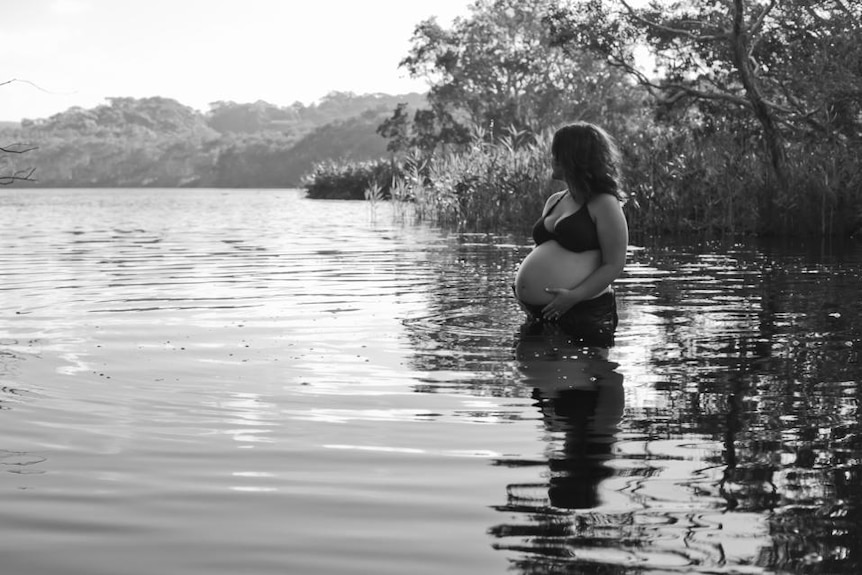 Black and white photo of pregnant woman in lake pictured in story about post natal body acceptance.