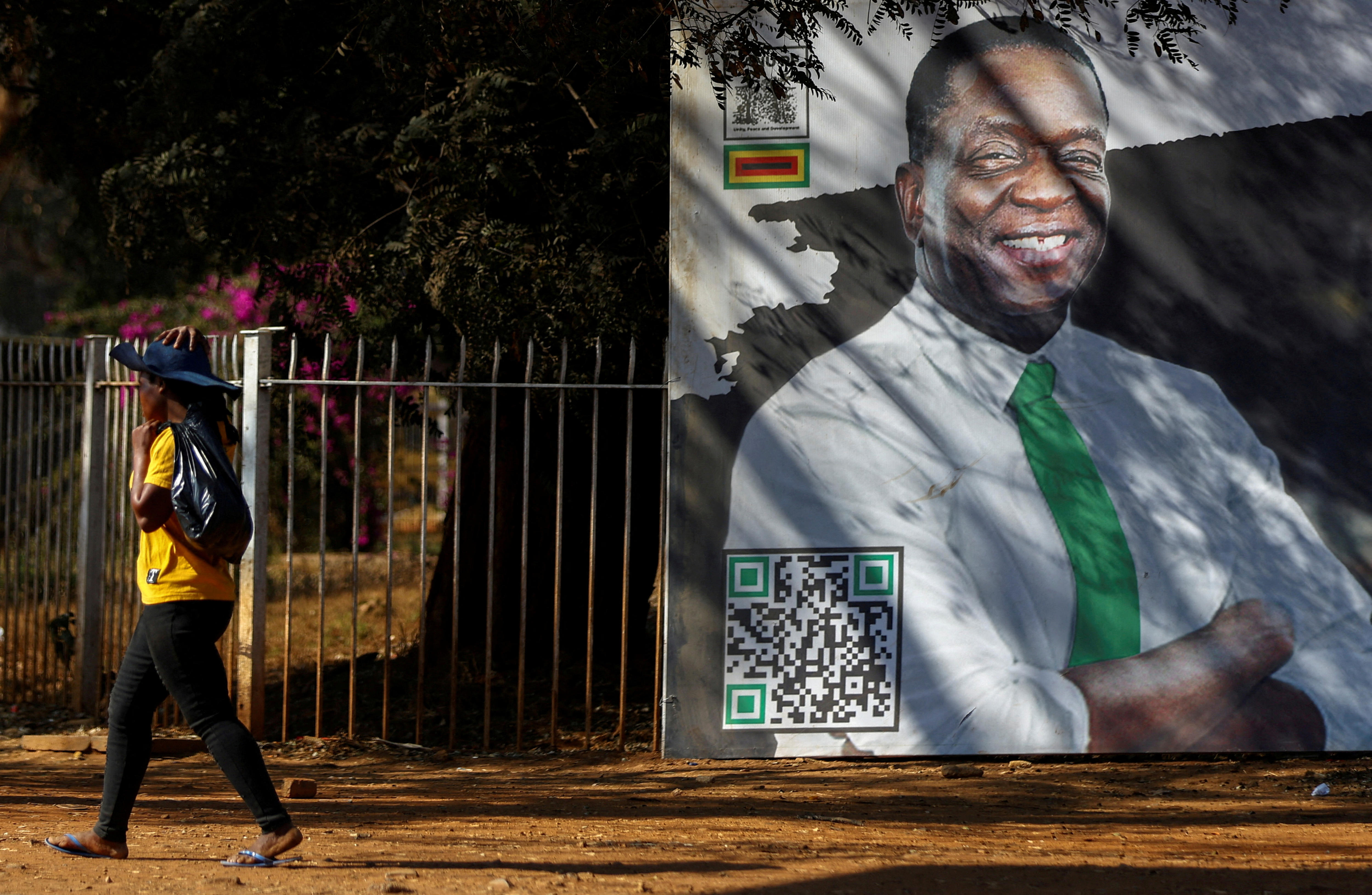 Man with arms crossed smile in billboard on wall as woman walks past. 