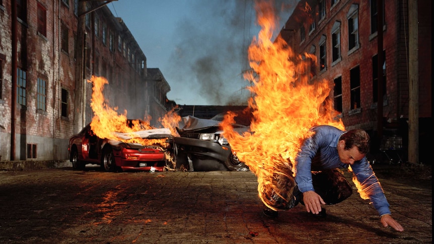 Man diving from a car that is on fire.