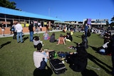 A crowd of people sitting and standing around a building with people speaking into a microphone