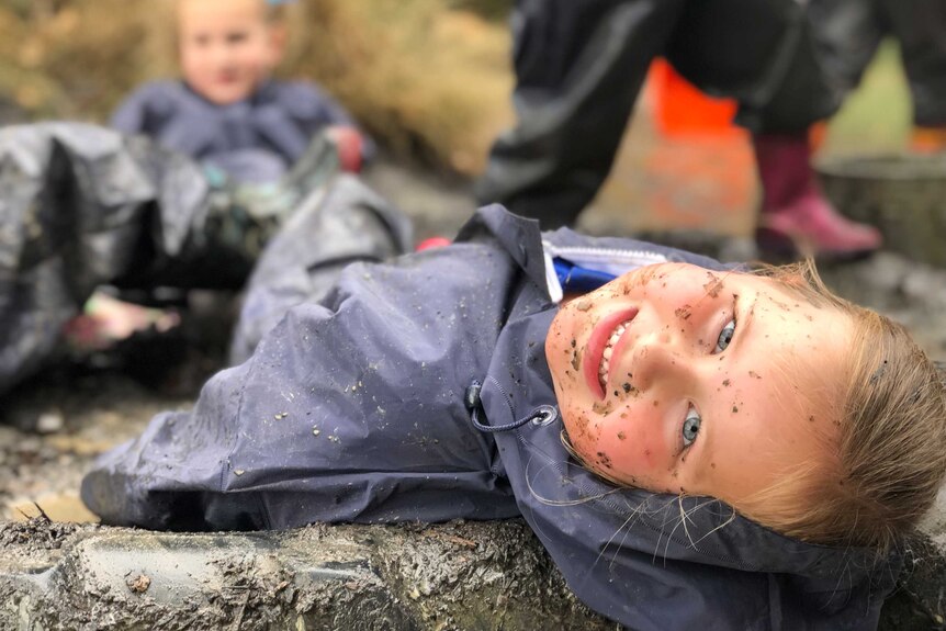 A smiling mud-splattered child lays back on the ground.
