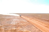 A truck driving on a desert road in the outback kicking up dust 