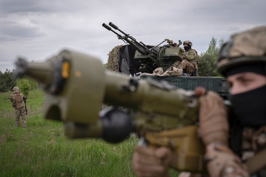 Members of a Ukrainian air-defense unit hold weapons in a field.