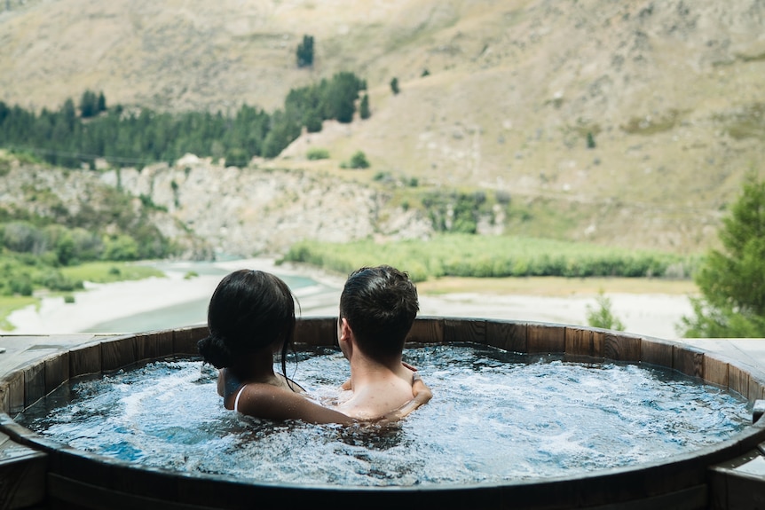 A couple embraces in a hot tub while looking out at a mountain range