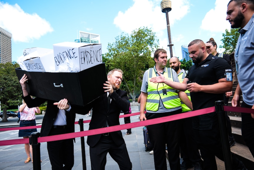 Two men in suits carry cardboard boxes labelled "evidence"