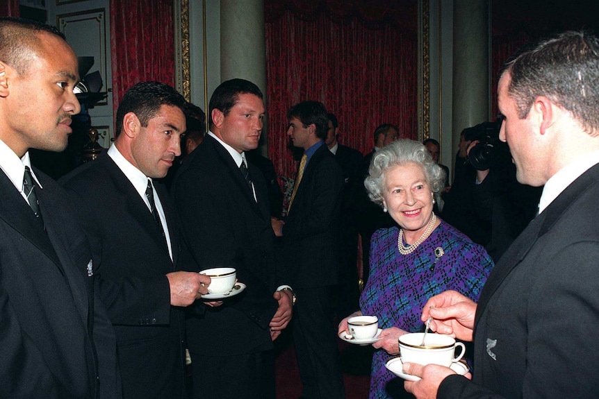 Queen Elizabeth drinking tea with All Blacks