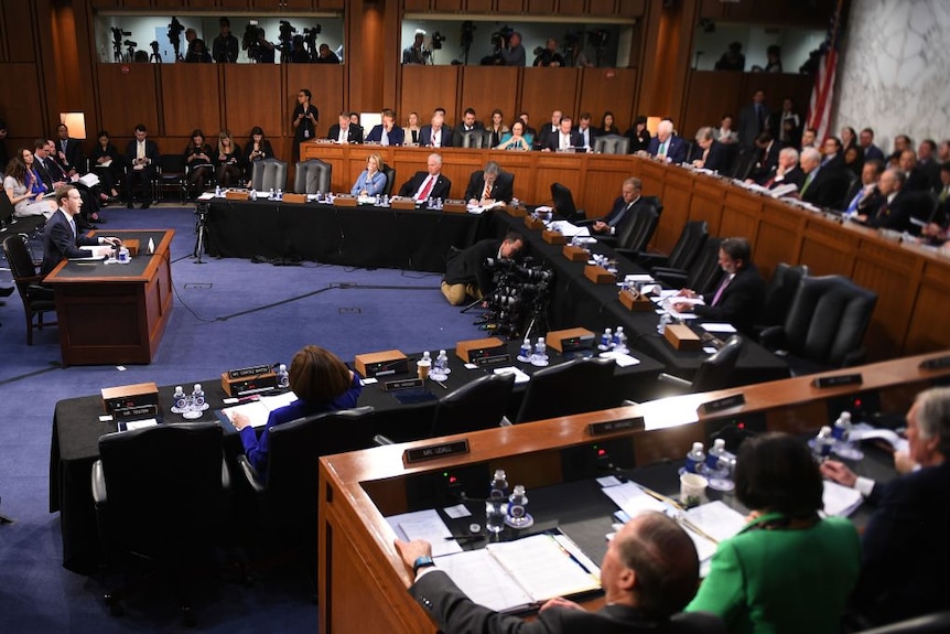 Facebook CEO Mark Zuckerberg sits before a special committee of congress and cameras.