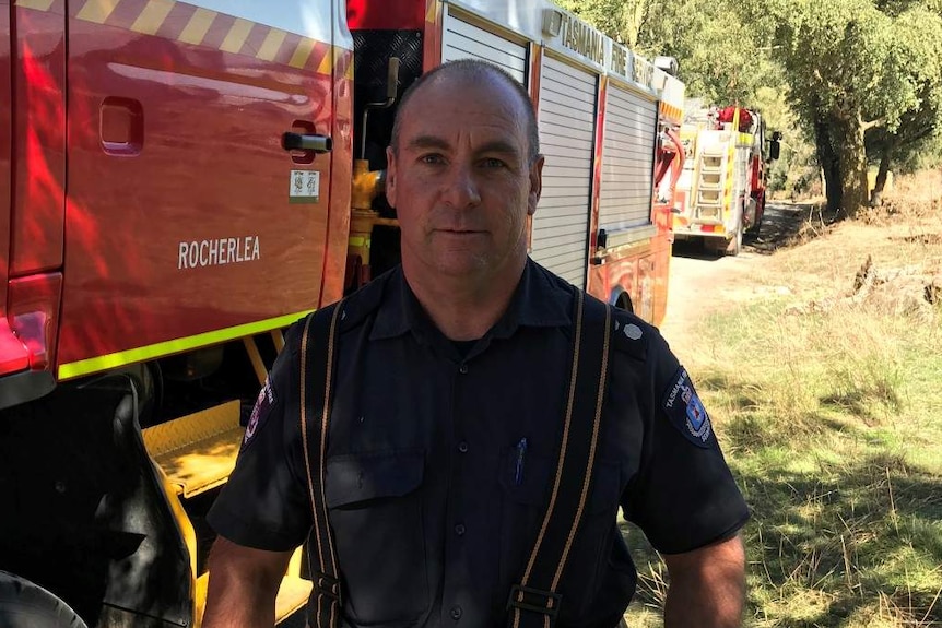 A firefighter stands next to a fire truck in a rural setting