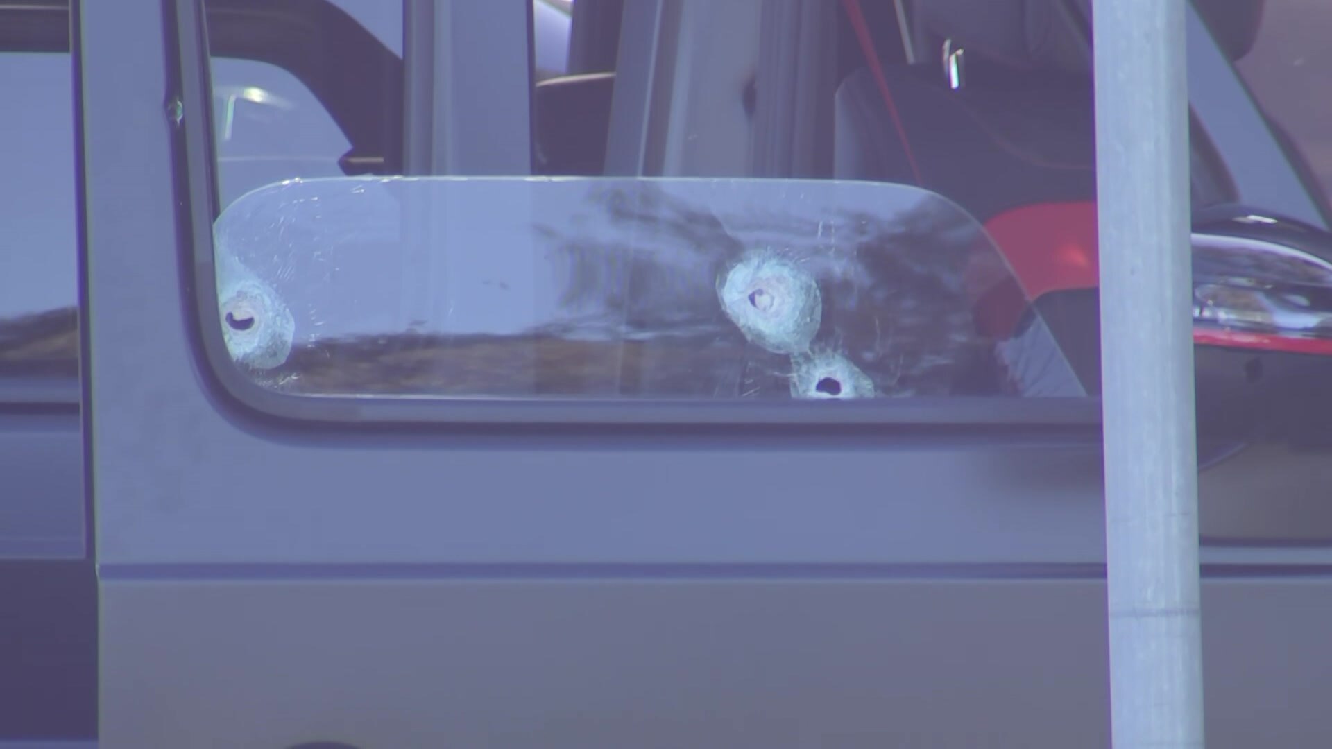 The side of a black car, with bullet holes visible in the driver-side window.