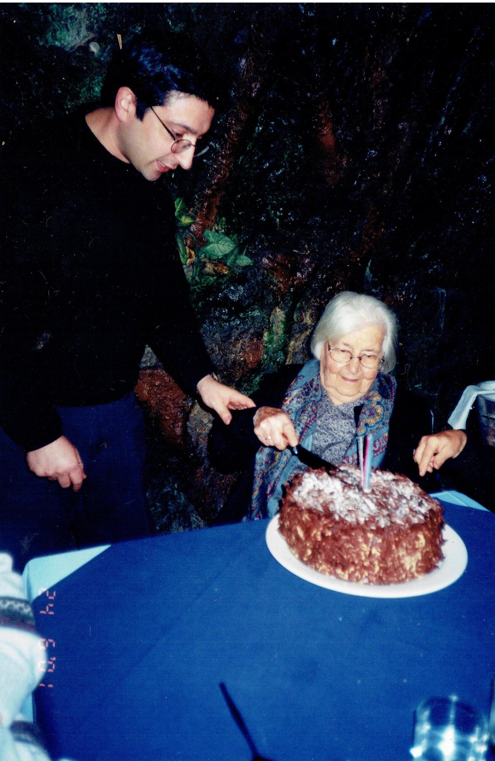 a historic picture of George Fotaras who co-owned Grotta Capri with his dad stands next to a woman cutting a cake