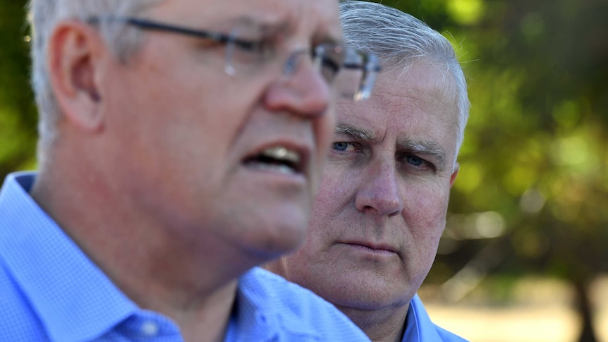 Michael McCormack watches Scott Morrison talk in an outdoor setting.