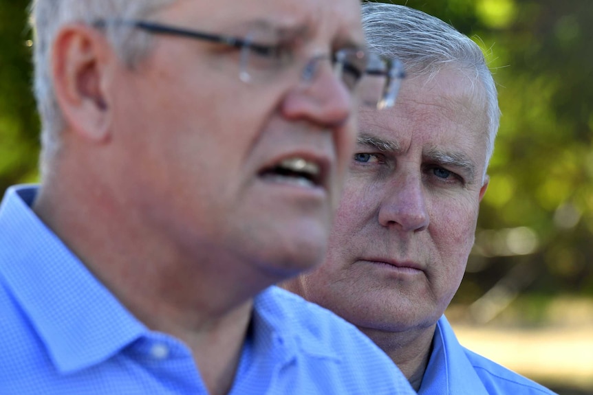 Michael McCormack watches Scott Morrison talk in an outdoor setting.