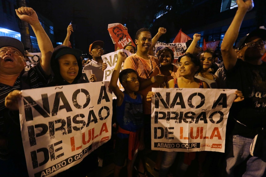 People holding signs that read in Portuguese "No to prison for Lula", waving hands.