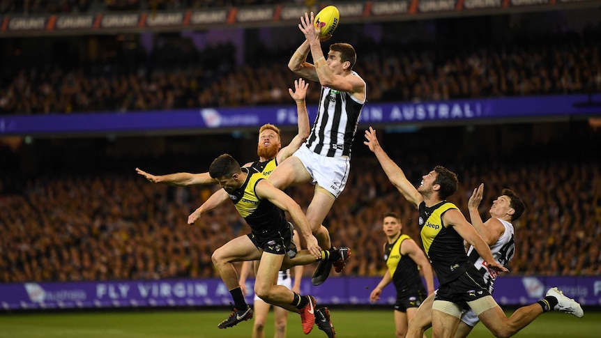 An AFL player flies for a mark in a pack at the MCG.