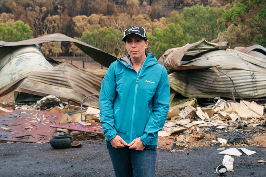 A woman in a blue tracksuit stands outside her burnt down home
