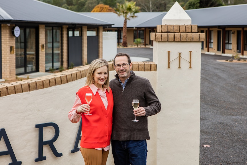 A couple smile champagne flutes in hand outside property gates 