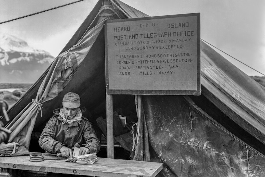 An old photograph of a man sitting outside a tent with a sign saying "post office" on Heard Island.