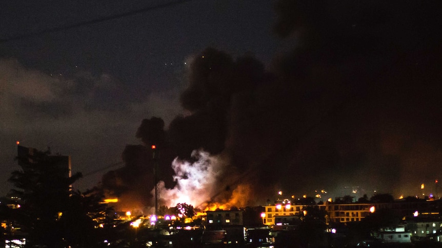 The flash of an explosion is pictured amid flames and smoke billowing from the National Assembly building in Libreville