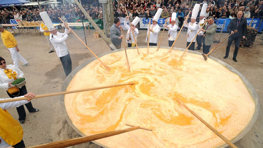 Chefs stand around a giant pan several metres wide stirring an egg mixture as they make their giant omelette.