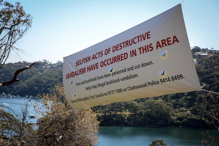 a banner that reads selfish acts of destructive vandalism have occurred in this area hanging up in bushland