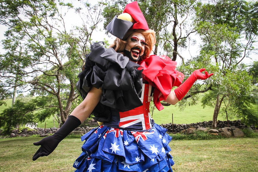 A man in drag smiles wearing an extravagant costume