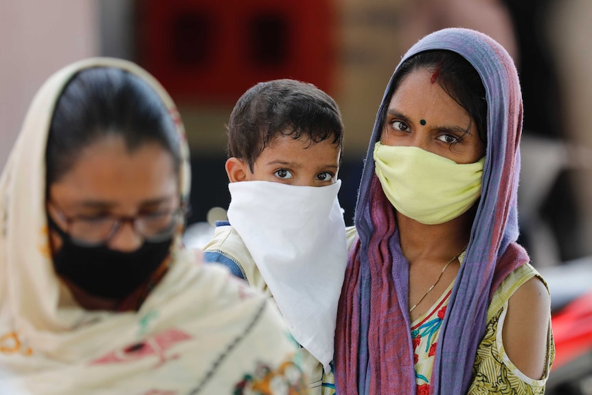 A woman carrying a child with both wearing colourful clothes and face masks.