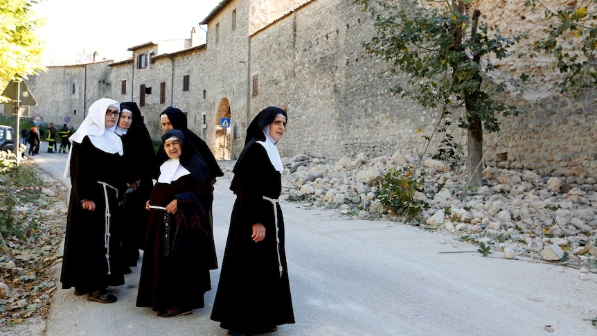 Nuns stand next a partially collapsed wall following earthquake