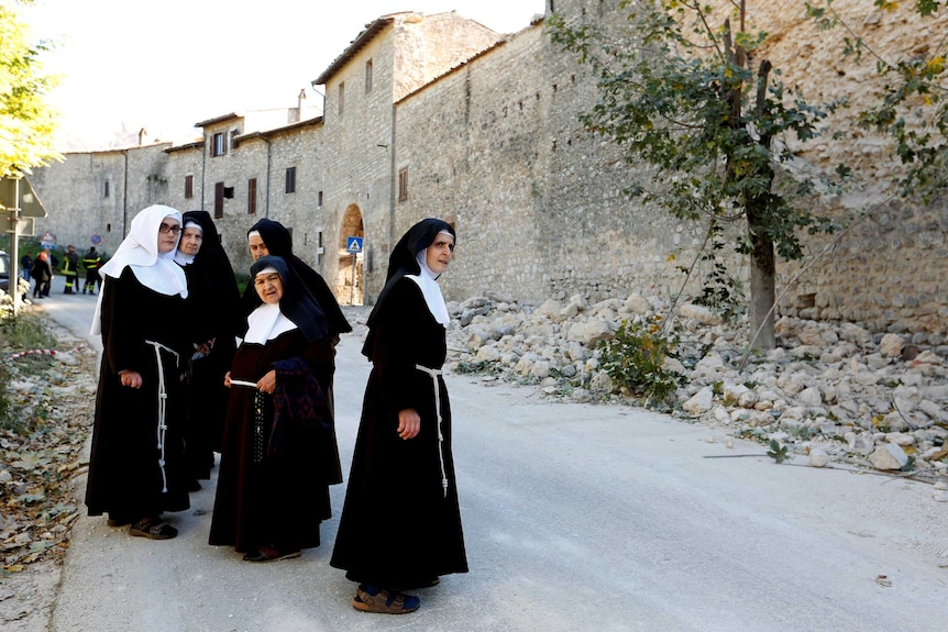Nuns stand next a partially collapsed wall following earthquake