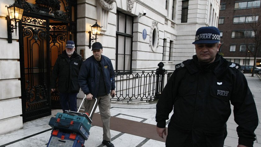 Police officers carry equipment as they leave a flat London