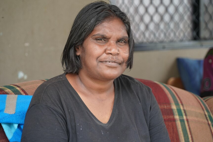 An Indigenous woman with shoulder-length hair, wearing a dark T-shirt and faintly smiling.