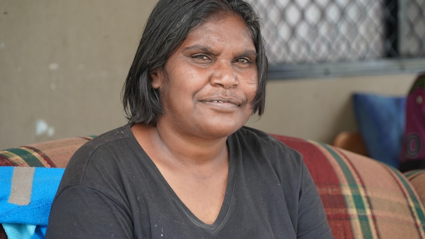 An Indigenous woman with shoulder-length hair, wearing a dark T-shirt and faintly smiling.