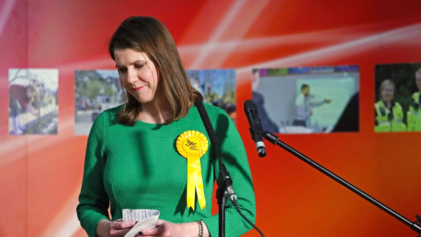 Jo Swinson looks forlorn as she stands behind a wooden lectern clutching hand-written notes as she prepares to leave the stage.