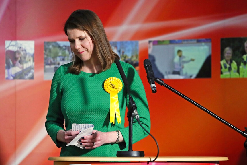 Jo Swinson looks forlorn as she stands behind a wooden lectern clutching hand-written notes as she prepares to leave the stage.