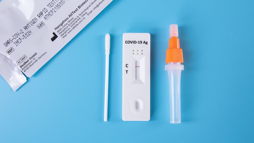 A generic image of a quick antigen test kit, a cotton swab, a droplet bottle and the test itself laid out on a blue surface.