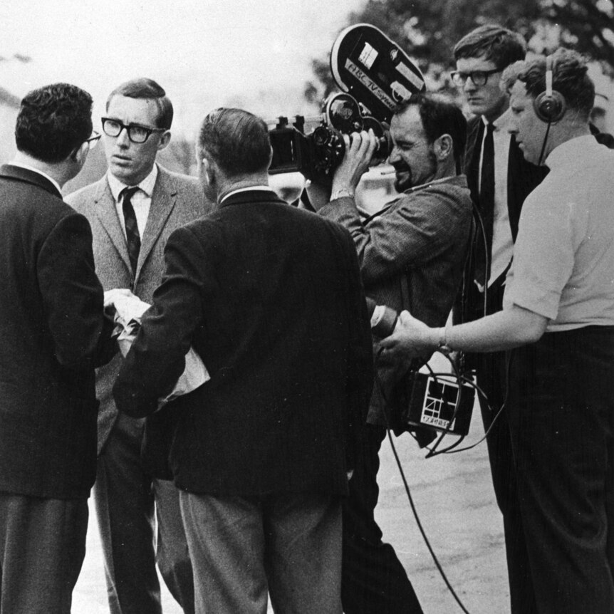 A person is interviewed, by a Four Corners crew, including a camera operator. All are wearing suits in the black and white photo