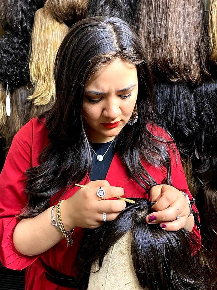 A woman with long black hair hand-making a human hair wig