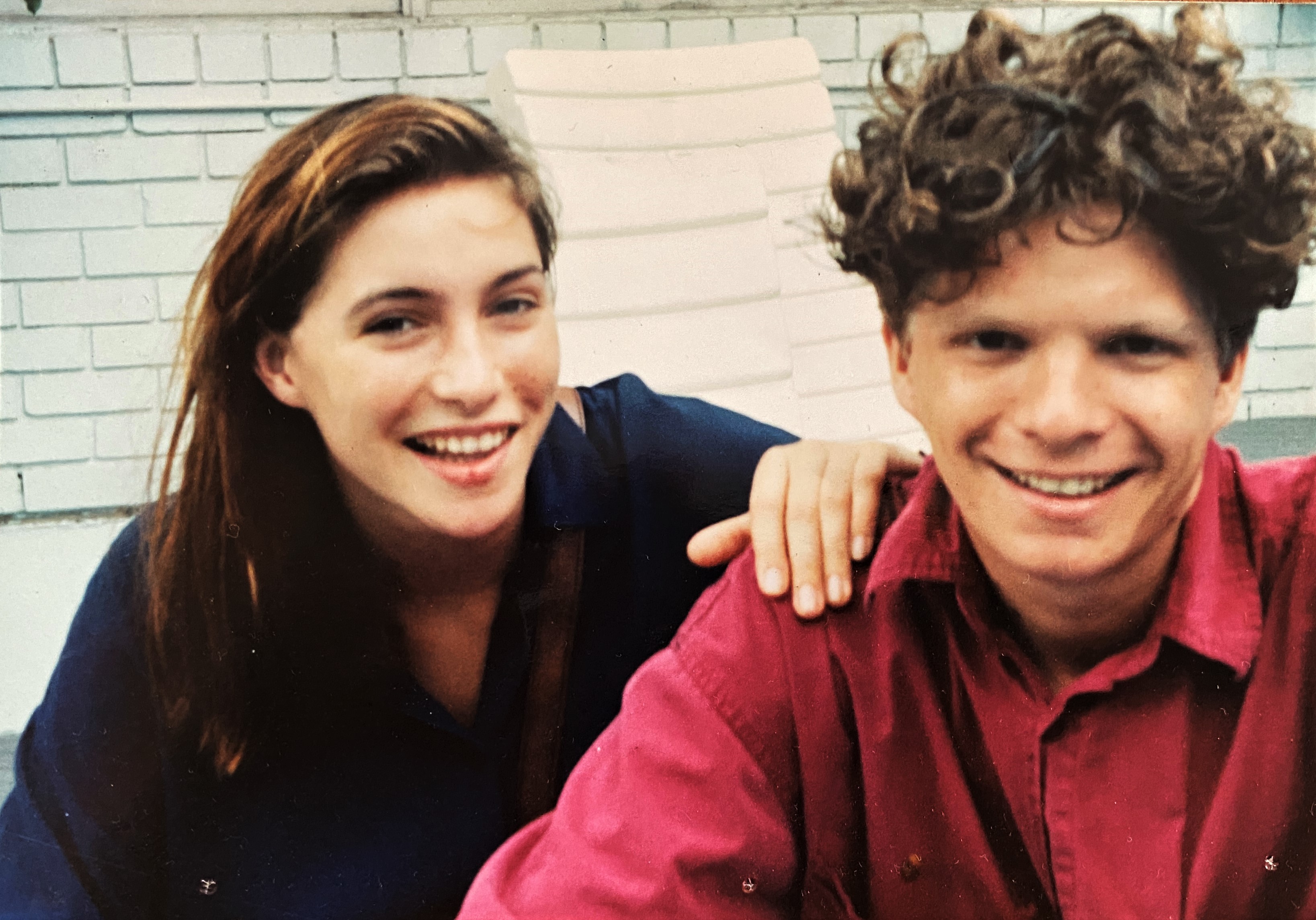 Claudia and Rupert in their 20s. She has her hand on his shoulder, and both are smiling at the camera.