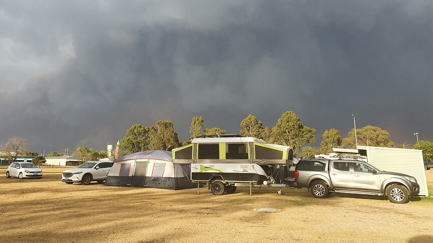 Cars and tents sit on dry grass below a black sky covered in thick smoke.