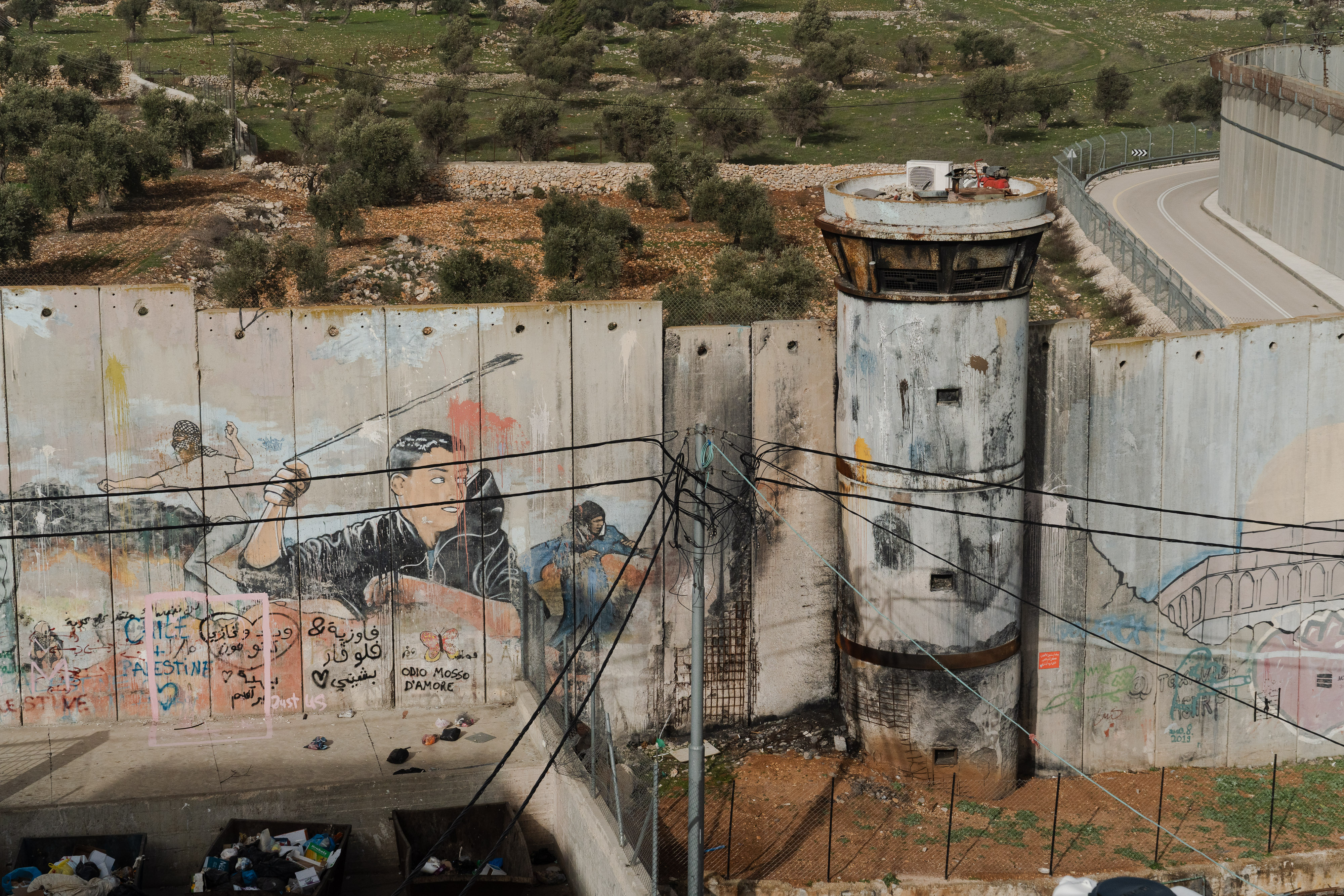 Una gran pared divisoria de hormigón cubierta de graffiti con una torre de vigilancia a la derecha.